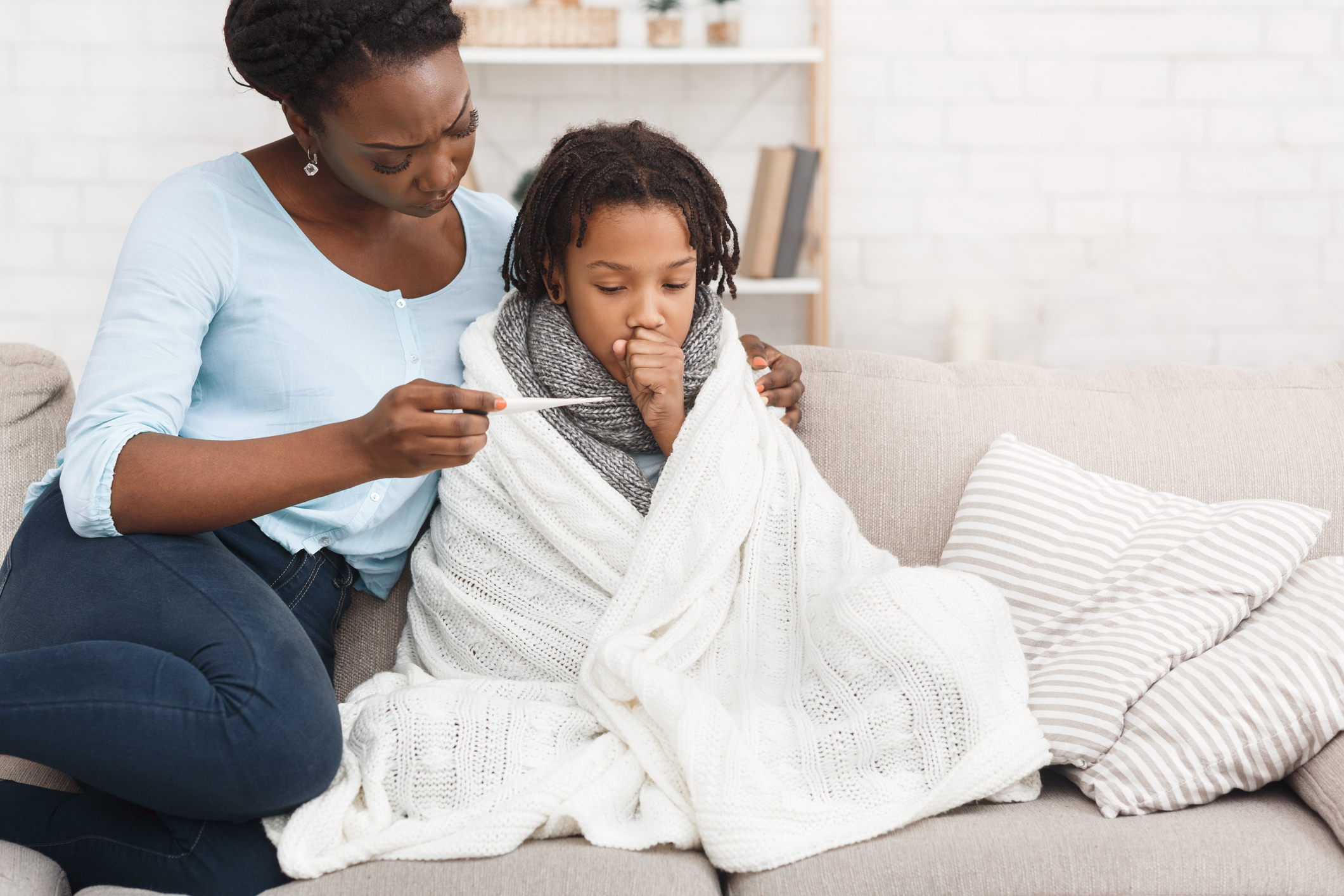 A mother looking concerned at a thermometer with her child whose bundled up in a blanket