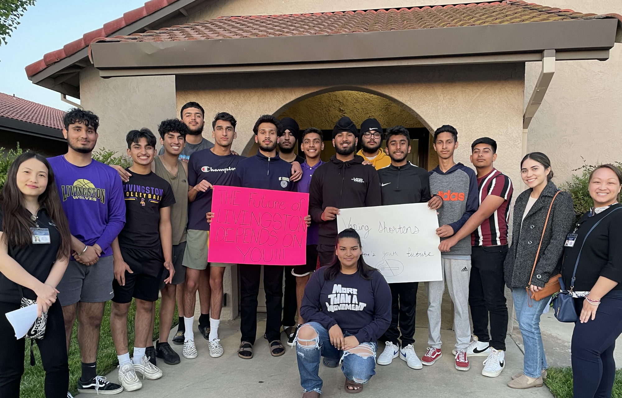 A large group of young people stands in front of a government building displaying signs 