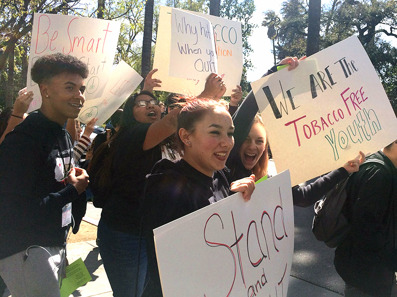 A group of smiling students marches and carries signs that say things like, “We are the tobacco free youth.