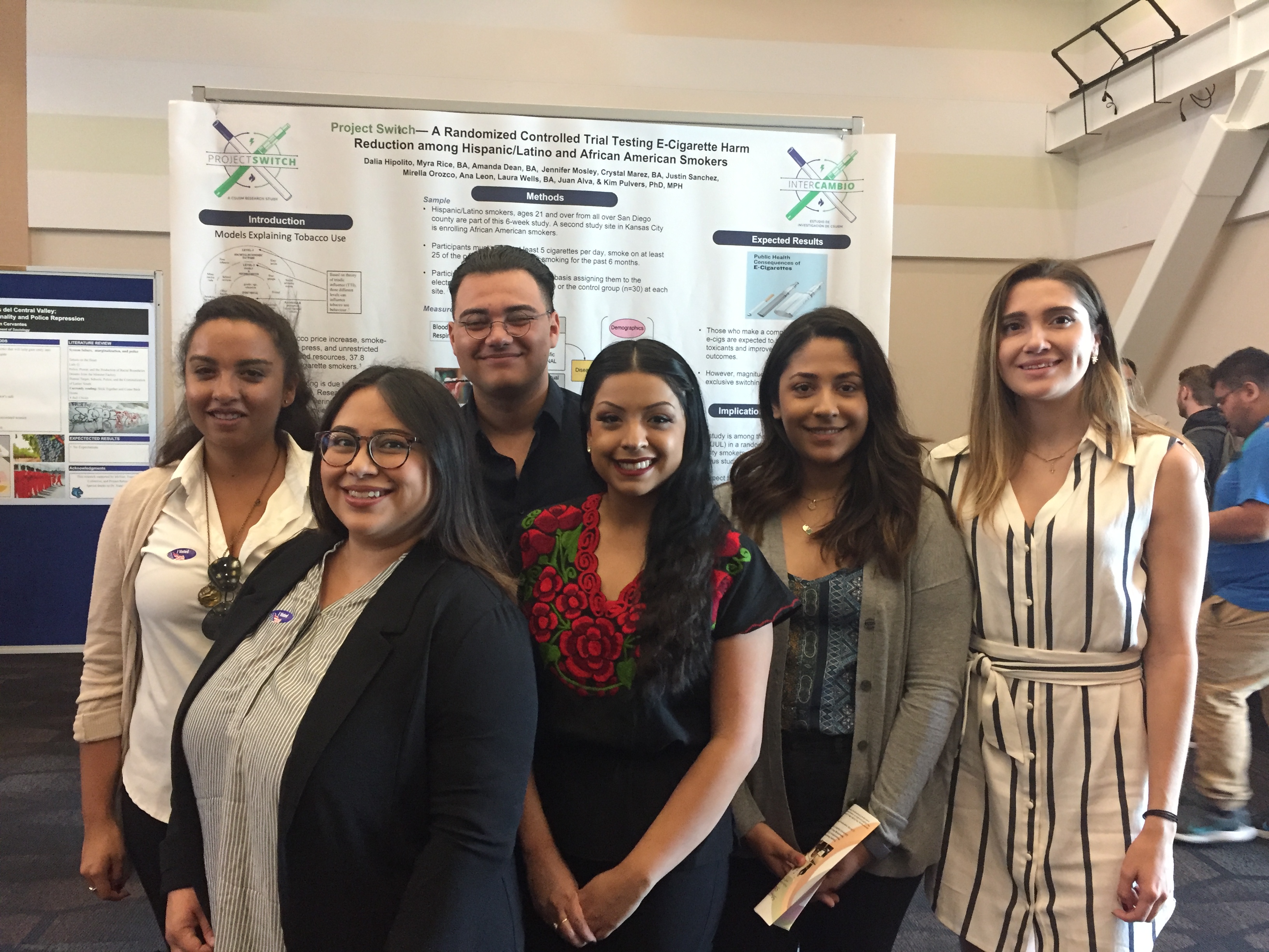 Six smiling college students stand in front of a poster at a scientific conference. The poster is entitled “Project Switch—A Ran
