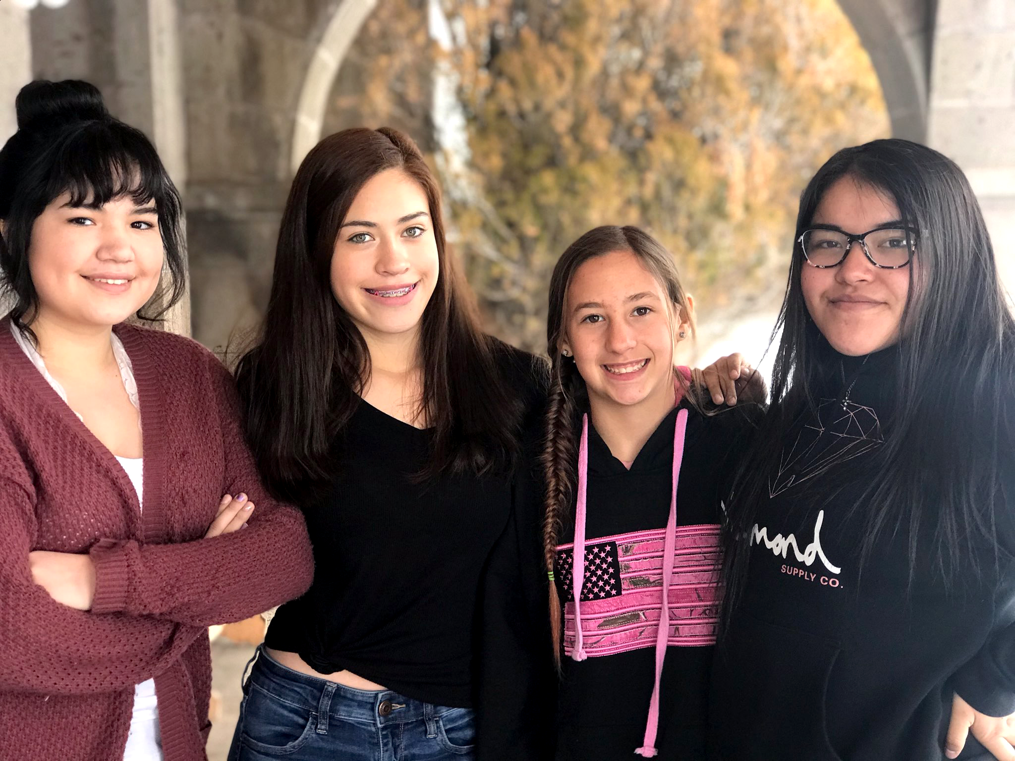 Four smiling high school students stand in a row under a stone arch.