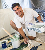 Home painter kneeling beside cans of paint at a work site