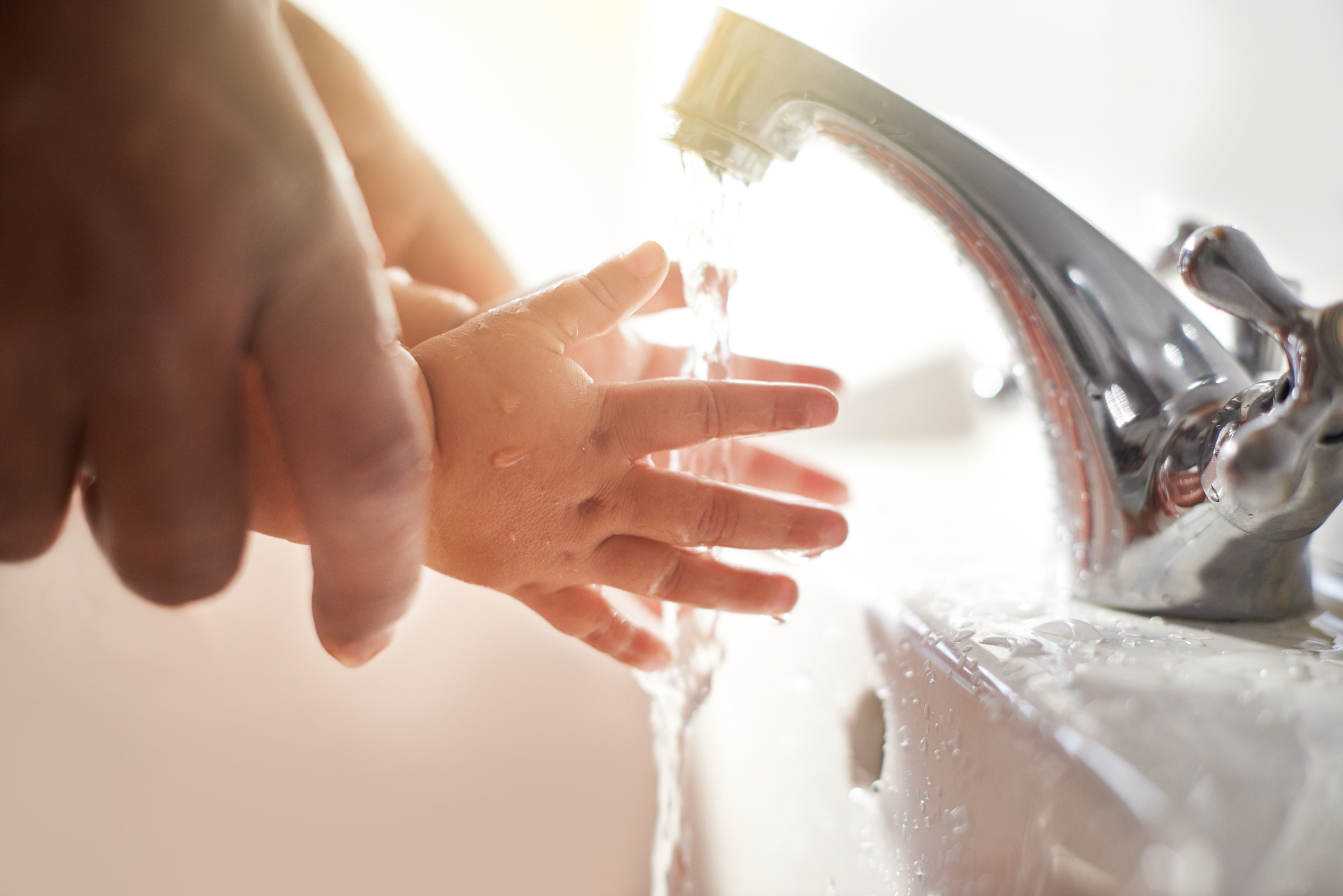 Close-up of toddler and adult washing hands.