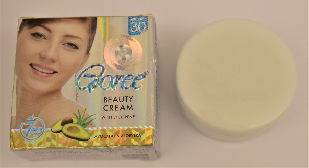 A round beige container of face cream next to its gold and beige box with a woman's face on it and blue lettering says "Goree"