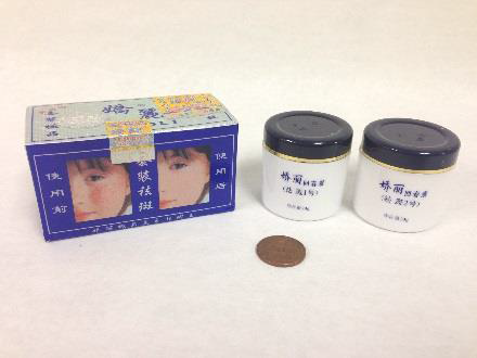 two round containers of face cream with white bottoms and black caps next to its blue box with a before and after picture 