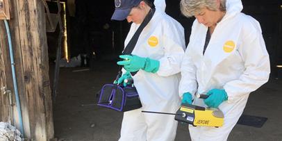 Investigators in tyvek suits holding instruments in the field