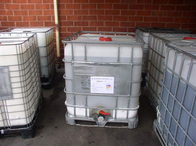 A large white plastic tub enclosed in a metal crate sits with similar tubs on the floor of a room with a red brick wall.