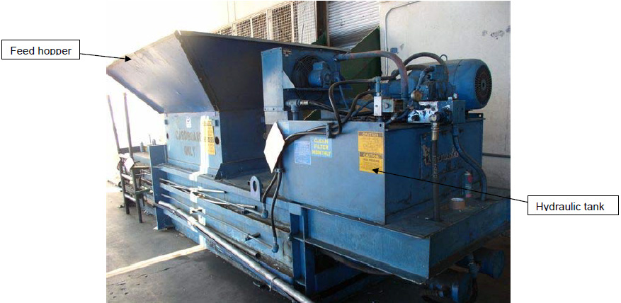 Side view showing large blue inverted pyramid metal opening on top. The machine housing is on the right with hydraulic lines running out of a metal box.