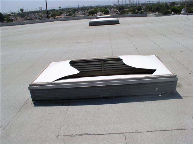 A skylight on a white rooftop. The covering is broken unevenly with jagged edges.