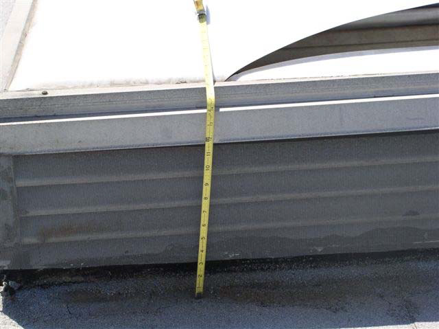 A measuring tape against the metal base of a skylight shows 15 inches of height from the rooftop to the skylight.