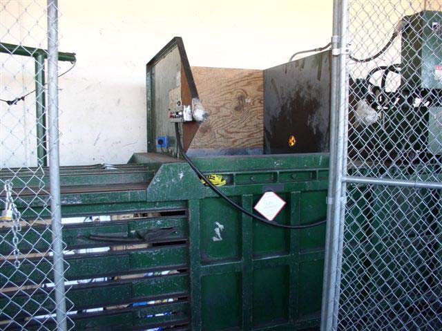 The middle of the large, green metal bailing machine with an opening at the top surrounded by two metal panels.