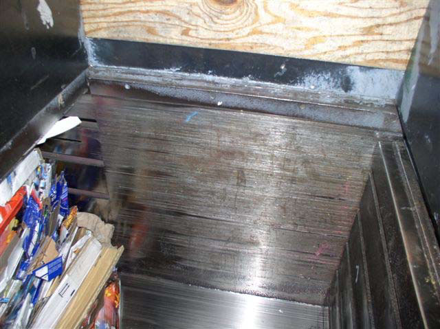 The inside of the bailing machine shows metal walls with signs of wear from the compactor pressing against them.