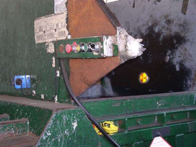 A control panel on the side of the metal machine has three buttons and a knob and is next to a triangular edge that is wrapped in tape and plastic.