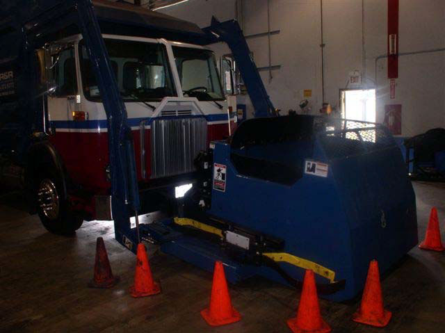 A large, blue metal bin is attached to the front of the truck by two long metal arms.