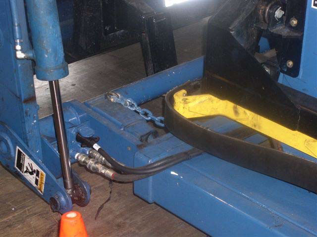 Three hoses are connected under a hydraulic cylinder and run underneath a pincher arm to the collection bin.