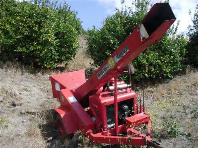A view of the front of the red wood chipper shows a long metal chute that juts diagonally away from the chipper and expels the chipped wood.