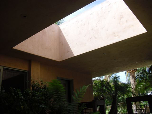 Close-up of roof opening seen from walkway below. The opening has smooth, sheer stucco sides with a stone patio beneath it.