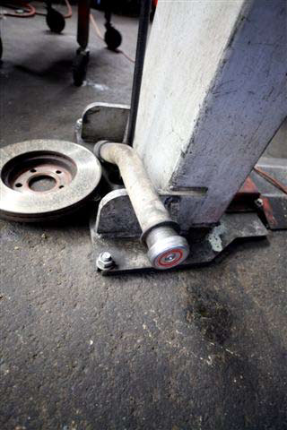 A metal fuel tank filling hose is on the ground next to an automobile brake and the base of an automobile lift device.