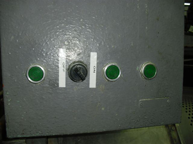 Closeup of horizontal control row with unlabeled green button on the left next to a black switch with an off label to the left and an on label to the right. There are two unlabeled green buttons to the right of the switch.
