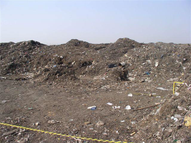 Mounds of dirt and trash surround a flat, dirt-filled area.