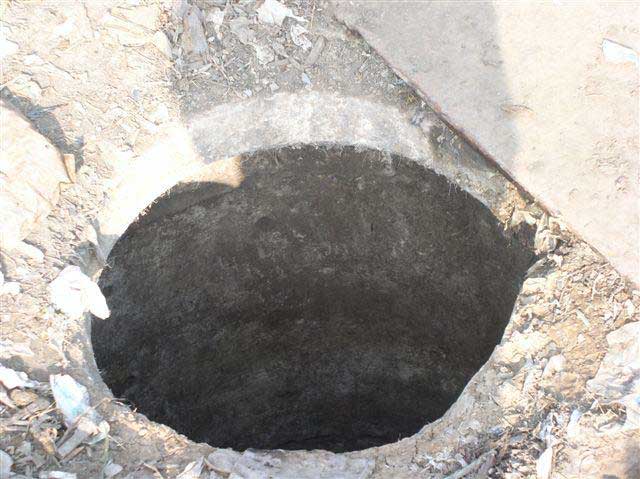 The concrete opening to the manhole shows the depth of the opening. A metal covering is placed to the right of the hole.