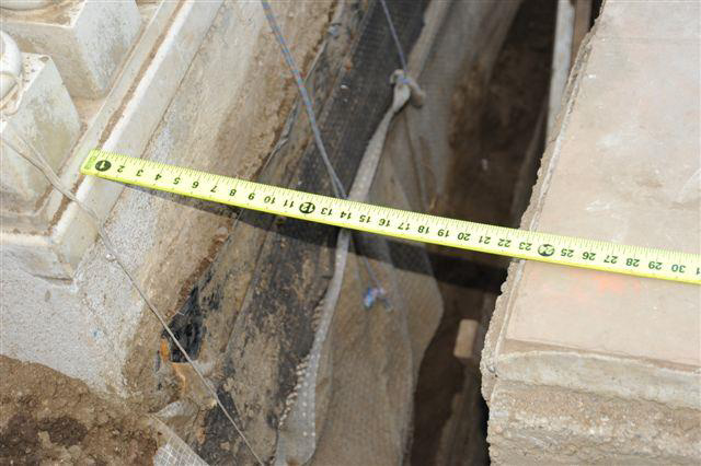 A tape measure across the very narrow trench, showing it is less than 2 feet wide.