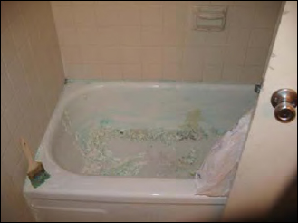 A bathtub with a paintbrush on the ledge and chemical paint remover rubbed on the sides.