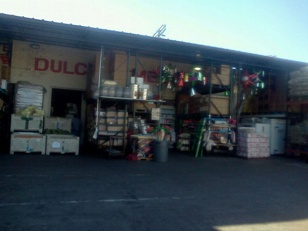 The outside part of a warehouse with the entry way surrounded by shelves stocked with boxes and loose items.