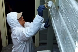 A worker applies a safer paint removal product to the wood exterior of a home.
