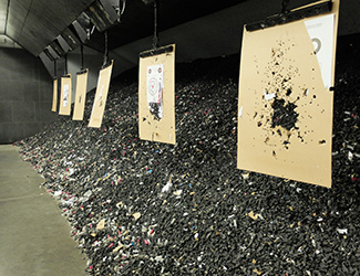 A pile of bullets and debris stands tall behind a row of hanging targets at an indoor shooting range.