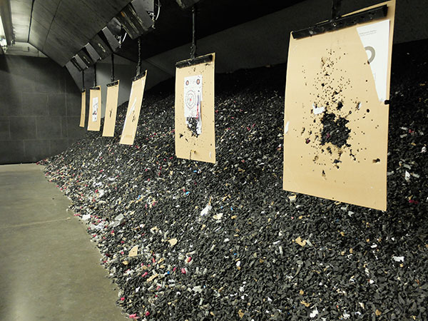 Shot-up target sheets hang from a shooting range with piles of bullets heaped behind the hanging sheets.