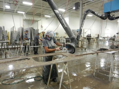 Worker sanding stone countertop in a large fabrication shop