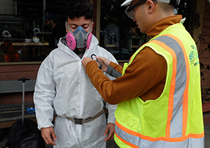 A worker attaches a lead cassette on a colleague for air monitoring
