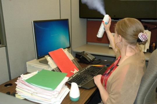 A worker sprays air freshener while sitting at her desk in an office