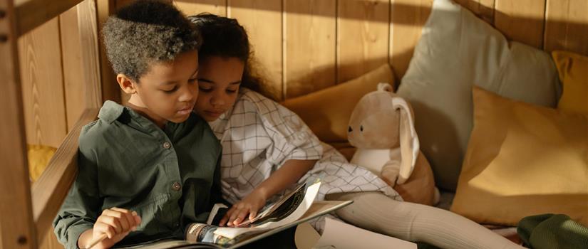 Two children read a book together while reclining