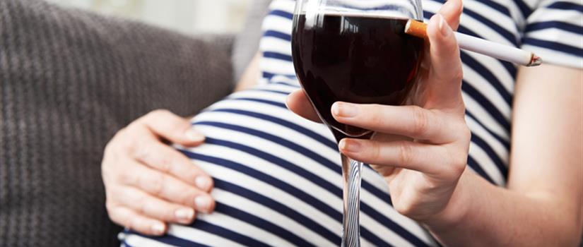 Pregnant individual holding a cigarette and glass of wine