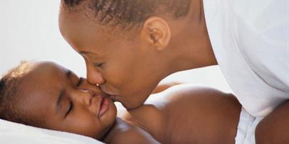 Black mother kissing her sleepy infant on cheek