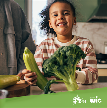 Child in kitchen, holding zucchini and broccoli