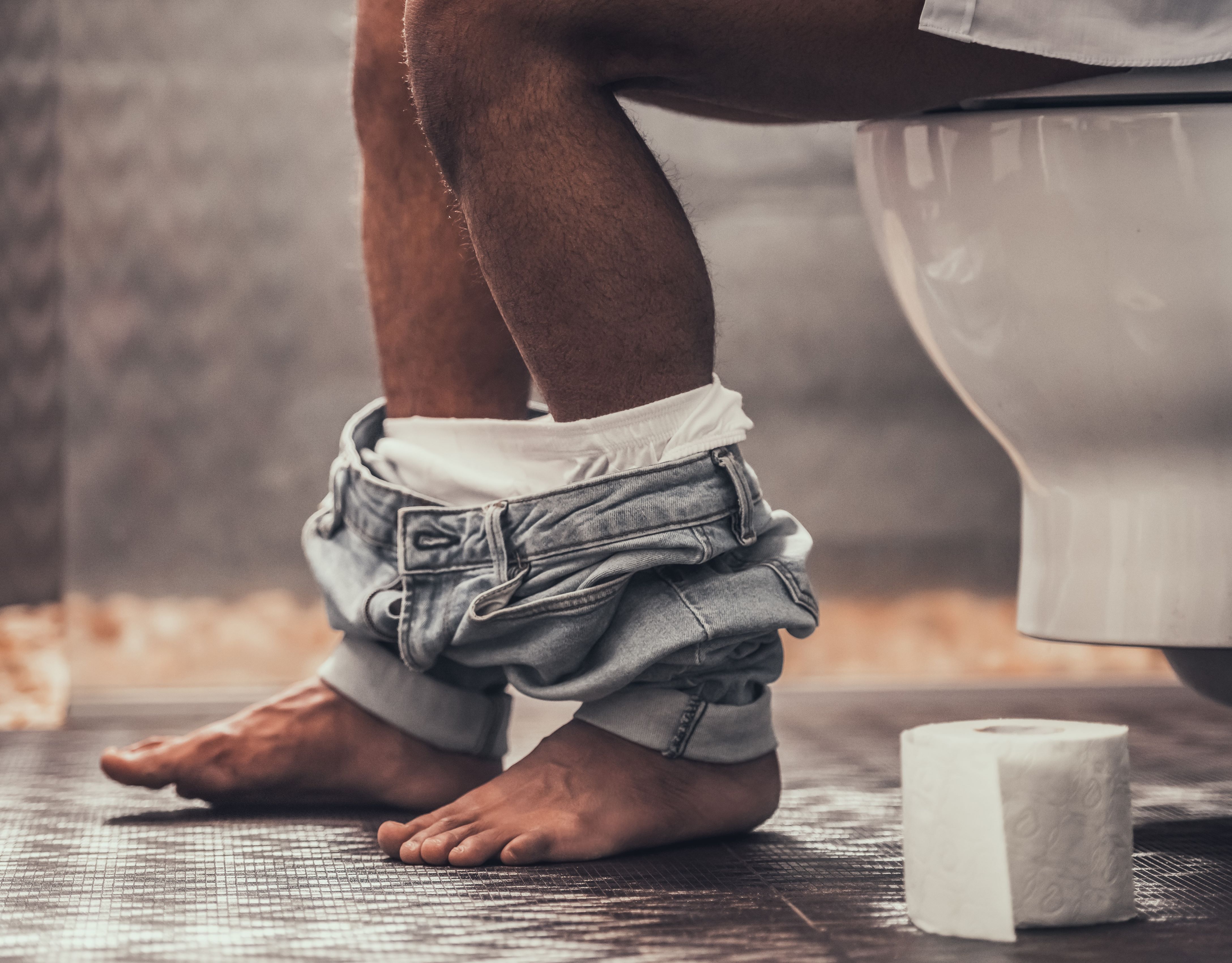 Person sitting on toilet with clothes around ankles.