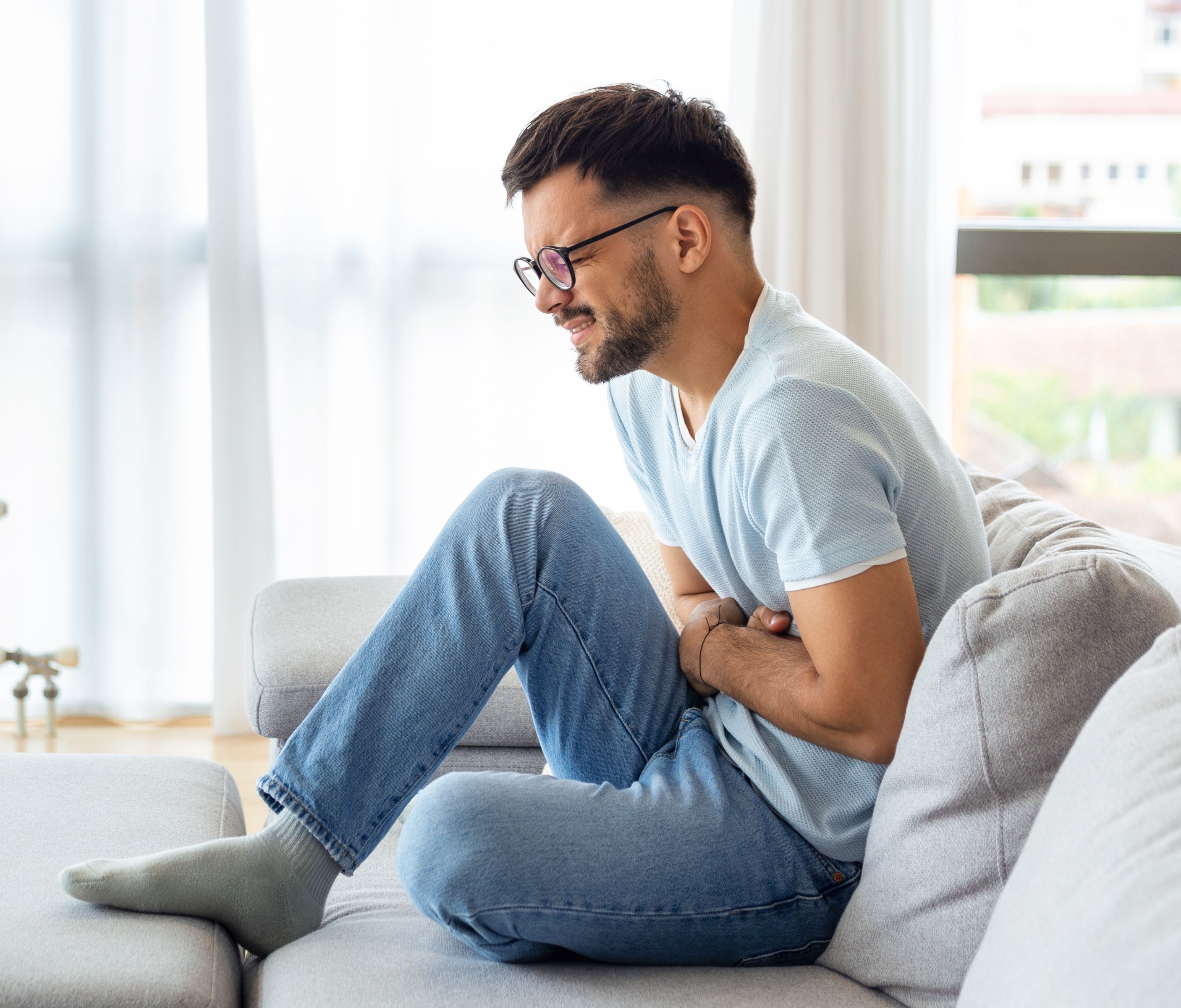 Man sitting on couch holding his stomach with look of discomfort on his face