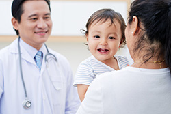 A young child smiles while being held by the mother during a visit to the doctor