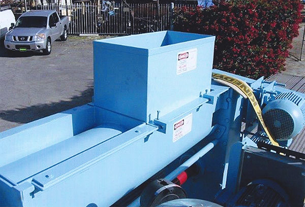 A large blue metal machine with a rectangular vent covering on top of it sits in a parking lot in an industrial area.