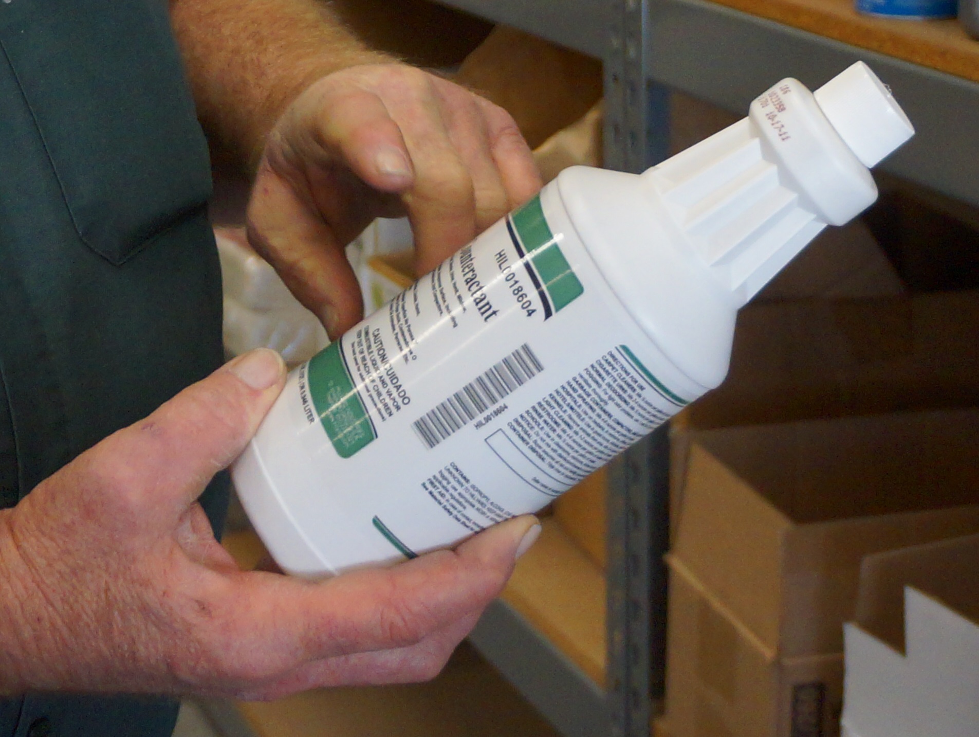 hands holding cleaning product bottle at an angle to read its ingredients hands holding cleaning product bottle at an angle to read its ingredients