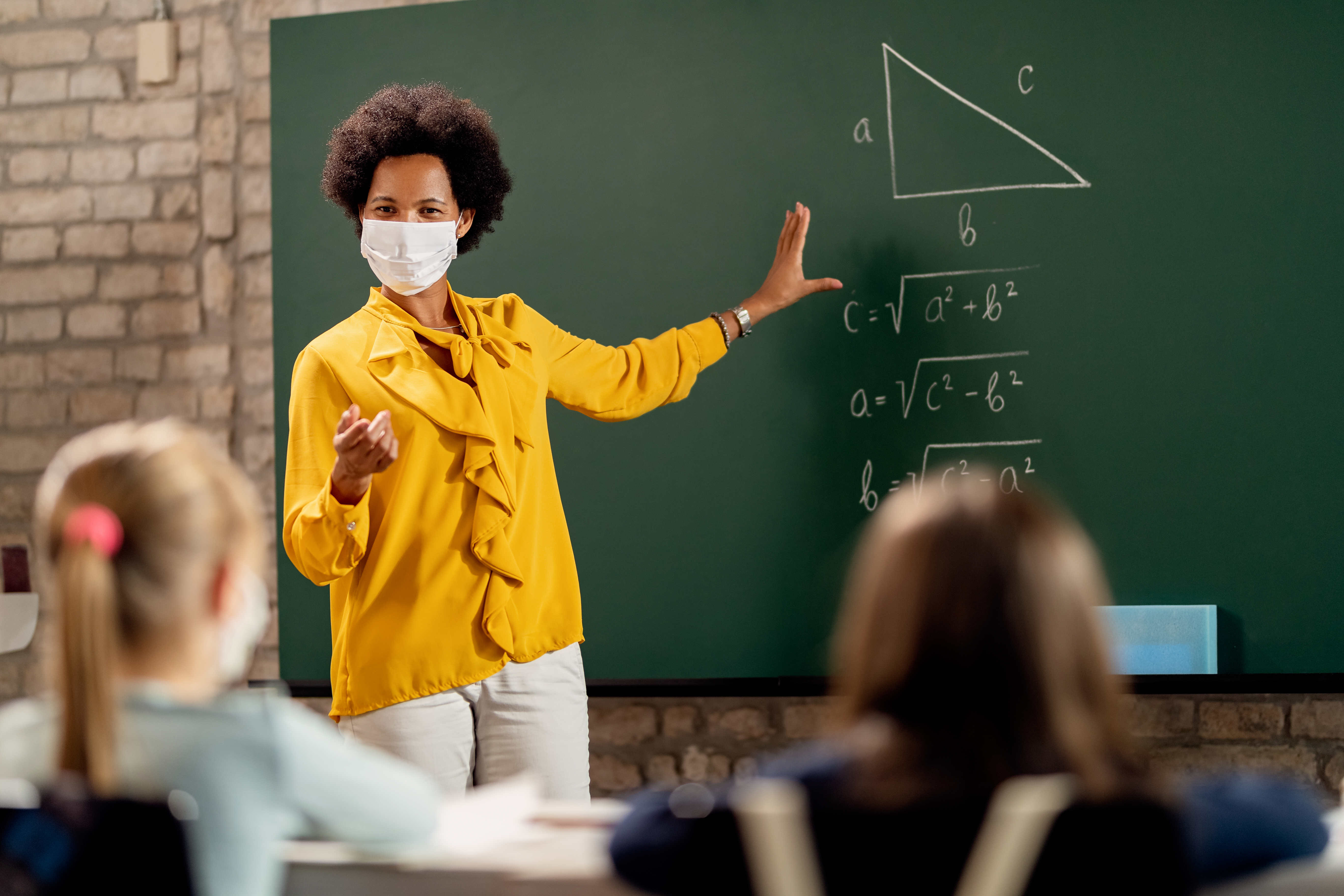 Teacher teaching in front of a black-board with mask